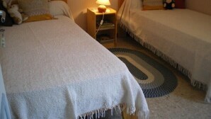 Ein Schlafzimmer mit zwei Einzelbetten, einem Nachttisch mit Lampe und einem kleinen Bücherregal.