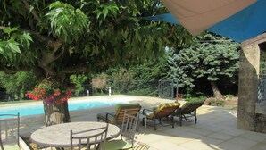 Ein Poolbereich mit rundem Tisch und Stühlen, umgeben von üppiger Vegetation und einem großen Baum.