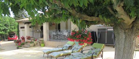 Une terrasse avec deux chaises longues, un arbre et un bâtiment doté d’un balcon.