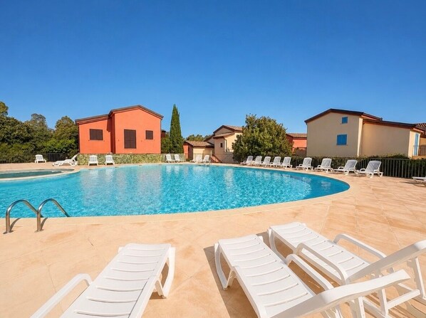 Une piscine avec des chaises longues, un ciel dégagé et des bâtiments en arrière-plan.