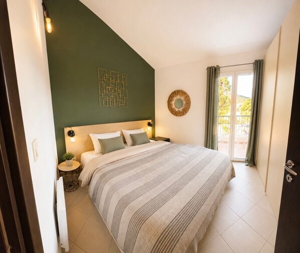 Ein Schlafzimmer mit einem Bett, Nachttischen, einem Wandbild, einem Fenster mit Vorhängen und Blick ins Freie.