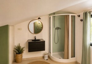 Ein Badezimmer mit einer Duschkabine aus gebogenem Glas, einem runden Spiegel, einem Waschbecken und einer Topfpflanze.