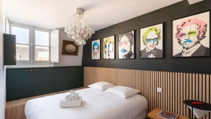 Ein Hotelzimmer mit Bett, einer Kandelaber, Kunstwerken an der Wand und einem Fenster.