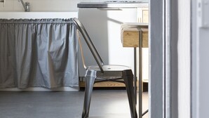A kitchen with white tiles, a wooden cabinet, and a metal chair. - L’Écume-Maison confortable et équipée (Saint-Coulomb)