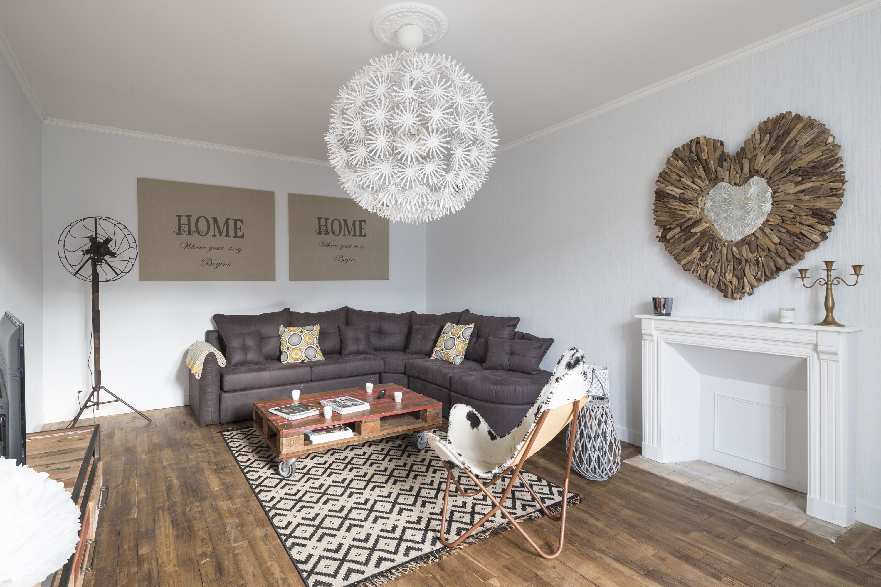 Ein Wohnzimmer mit einem Ecksofa, einem weißen Sessel, einem Kamin und einer dekorativen Wandgestaltung in Herzform.