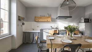 A modern kitchen with a wooden dining table set for six, a built-in oven, and a microwave. - L’Écume-Maison confortable et équipée (Saint-Coulomb)
