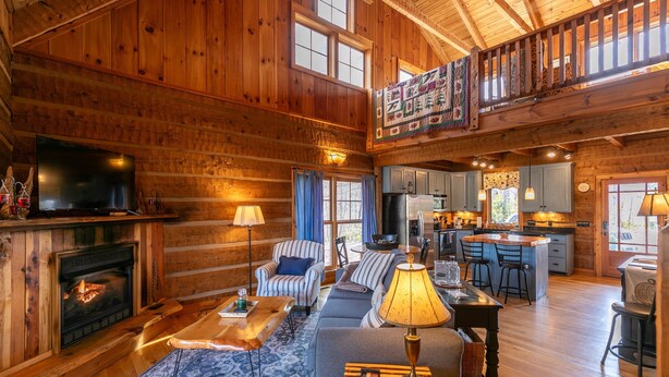 A spacious log cabin interior with a fireplace, a television, a sofa, and a dining area. - Walk in the Clouds - Rustic Cabin with Hot Tub, Outdoor fireplace, Fenced Dog Area (Boone)