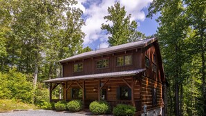 A two-story log cabin with a porch, surrounded by dense forest. - Walk in the Clouds - Rustic Cabin with Hot Tub, Outdoor fireplace, Fenced Dog Area (Boone)