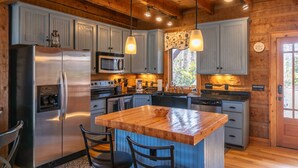 A modern kitchen with wooden cabinets, stainless steel appliances, and pendant lighting. - Walk in the Clouds - Rustic Cabin with Hot Tub, Outdoor fireplace, Fenced Dog Area (Boone)