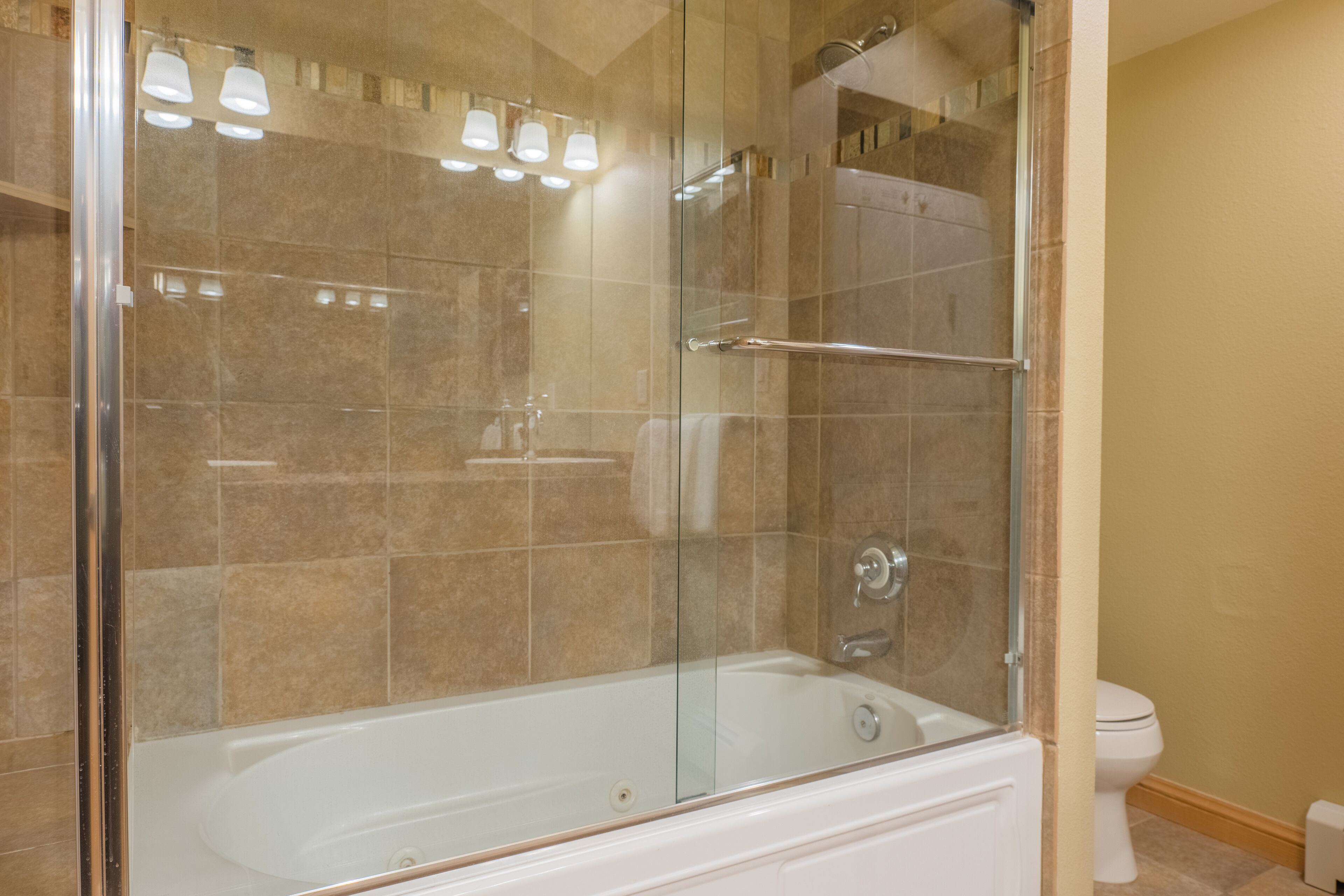 A modern bathroom with a glass-enclosed shower, a white bathtub, and a beige tiled wall.