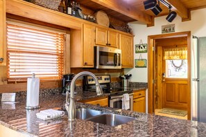 A kitchen with granite countertops, stainless steel appliances, wooden cabinets, and a window with blinds.