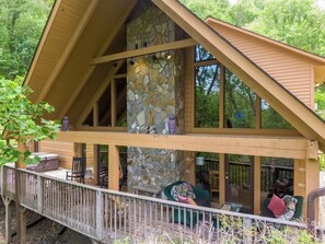 Eine Holzhütte mit Steinkamin, einer Holzterrasse und einem großen Fenster mit Blick auf einen Wald.