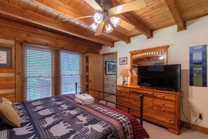 A room with a bed, wooden dresser, television, and a ceiling fan.