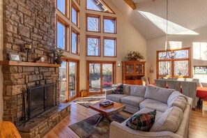 A spacious living room with a stone fireplace, large windows, and a cozy seating area. - Great Escape - Wood fireplace, mountain views, access to tennis courts, pool, and more (Boone)