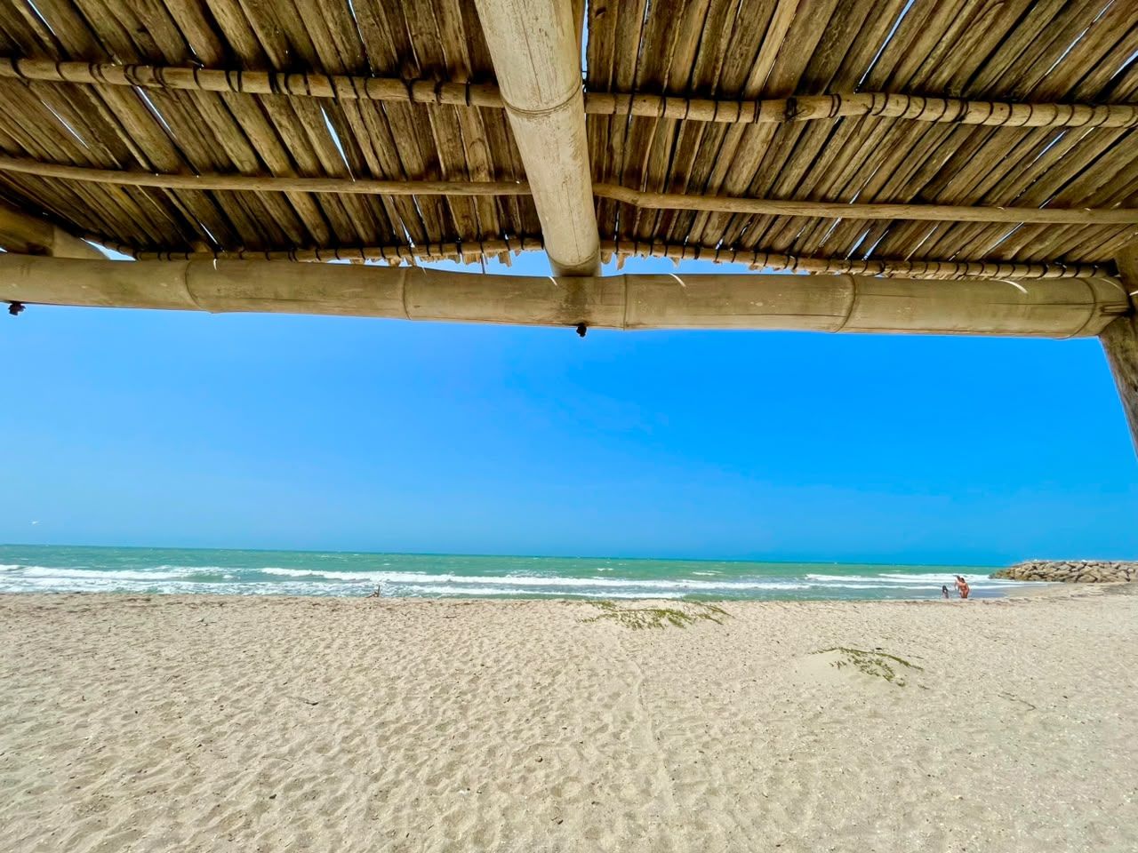 Une plage avec une structure dotée d’un toit de chaume, une plage de sable et une vue sur l’océan.