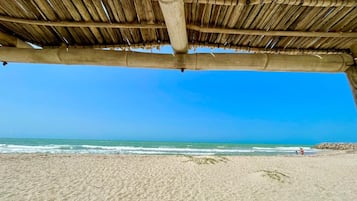 Une plage avec une structure dotée d’un toit de chaume, une plage de sable et une vue sur l’océan.