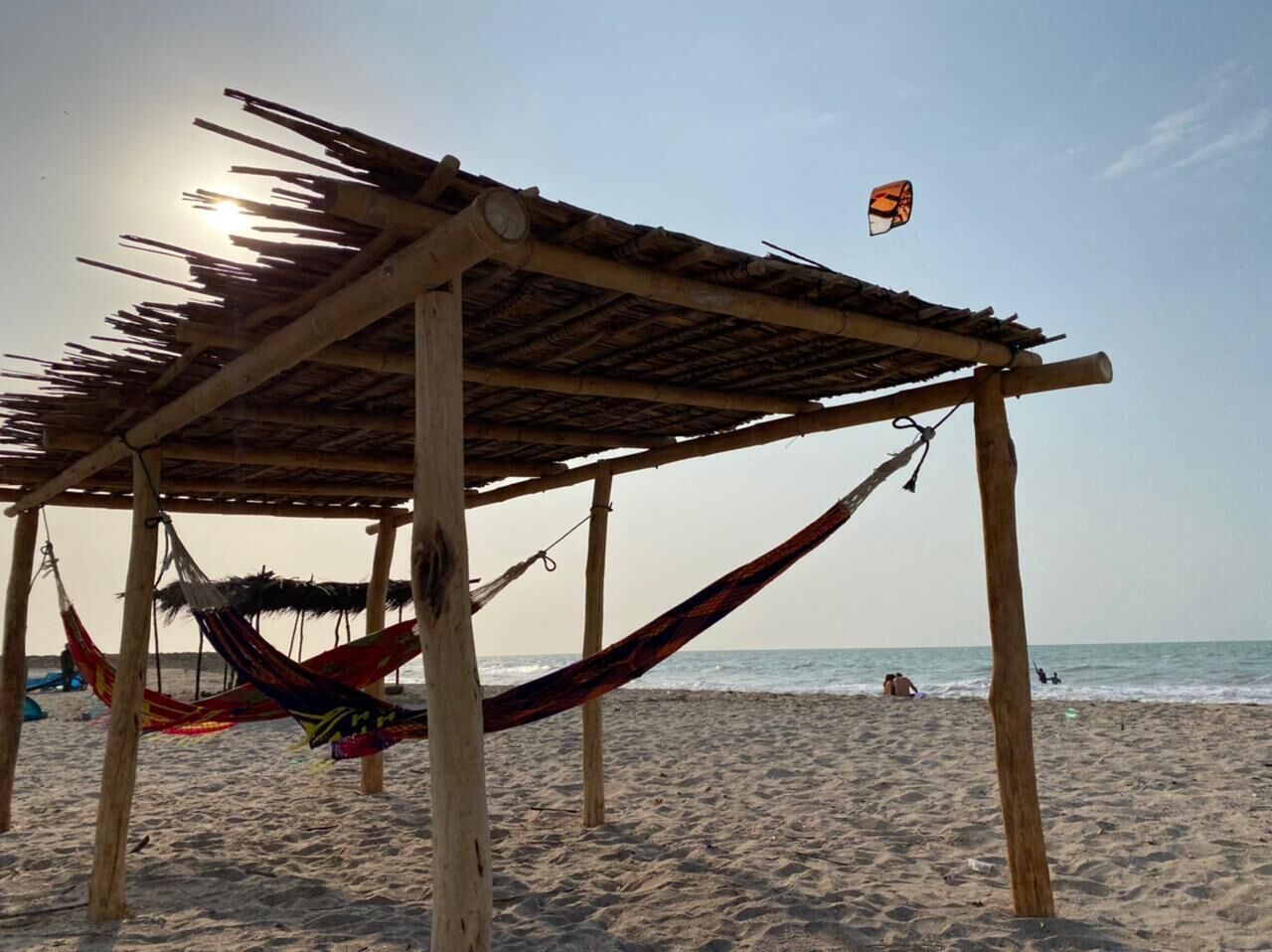 Ein Strand mit einer Holzkonstruktion, einer Hängematte und einer Person im Wasser.
