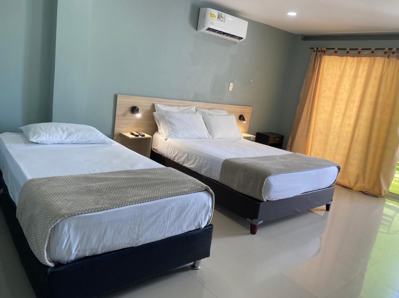 Quarto de hotel com duas camas, uma cabeceira de madeira, luminárias de cabeceira e um ar condicionado.