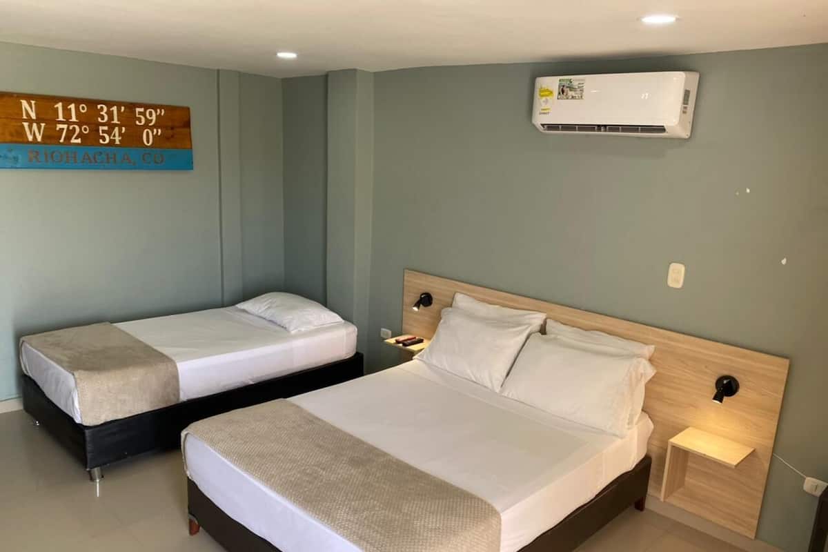 Habitación de hotel con dos camas, aire acondicionado de pared y una mesita de noche con lámpara.