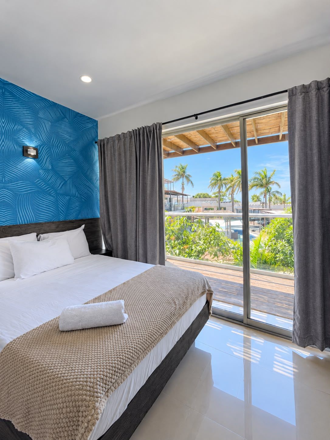 A modern hotel room with a large bed, a view of palm trees, and a balcony.