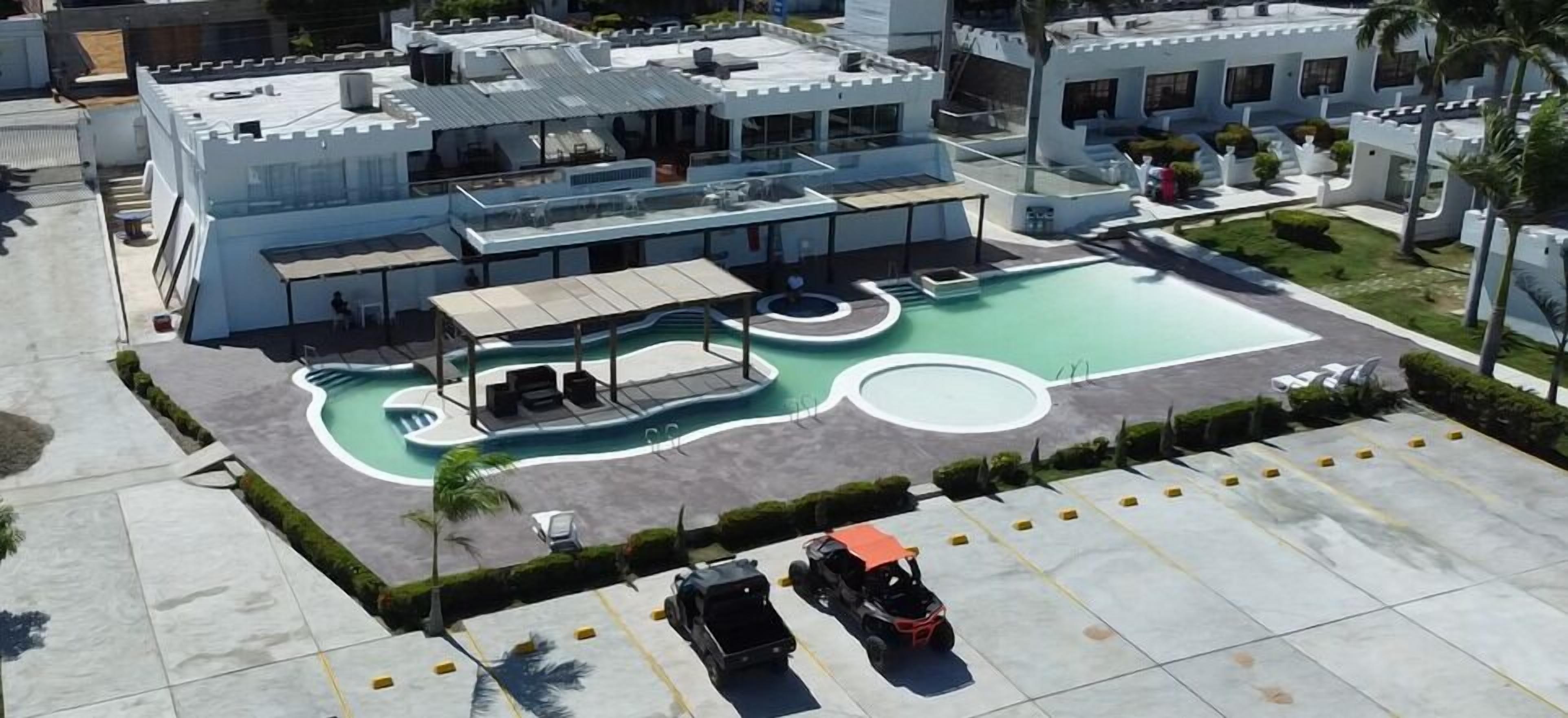 A modern hotel with a rooftop pool, outdoor seating, and a parking area.