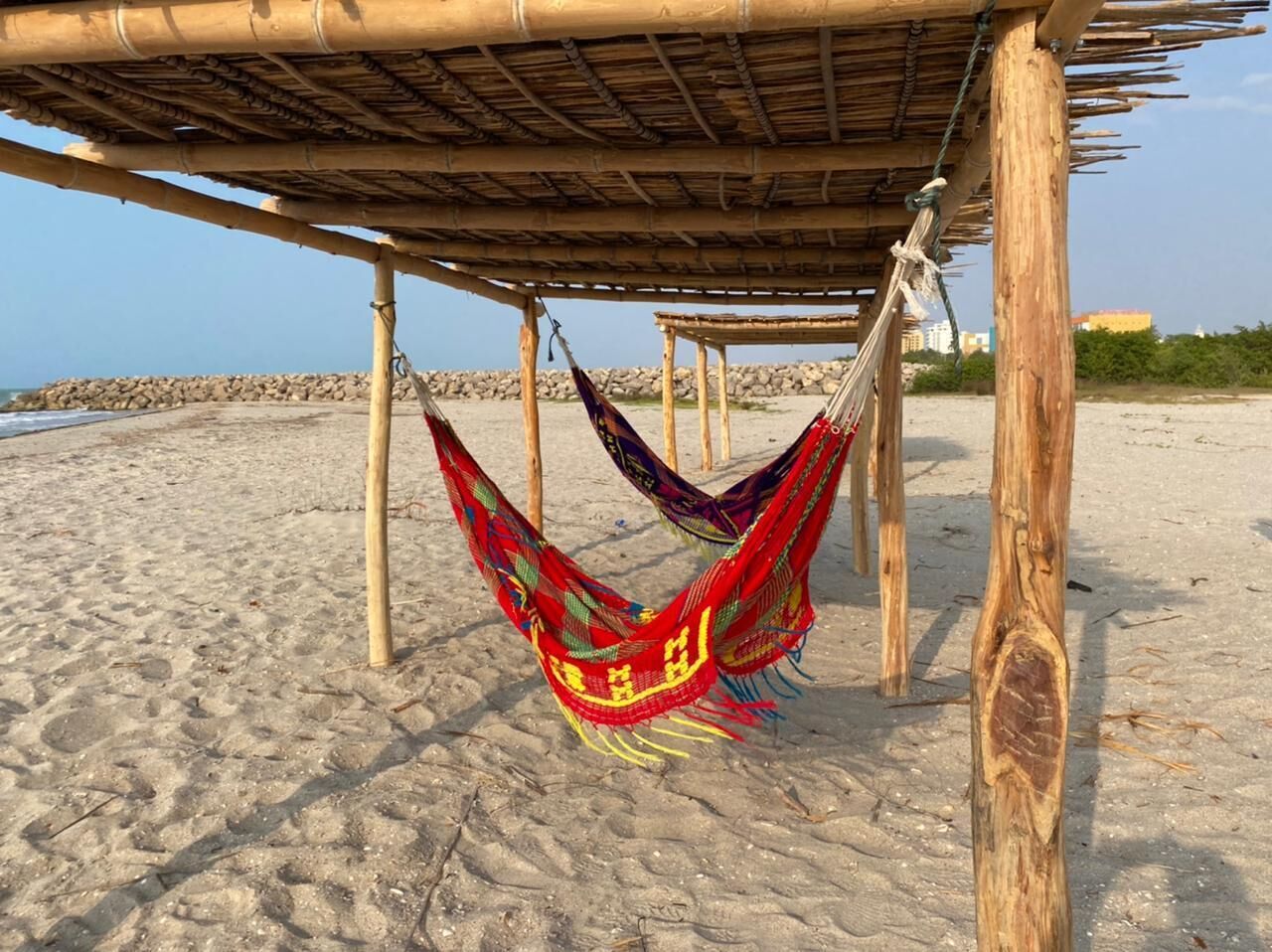 A hammock under a bamboo structure on a sandy beach.