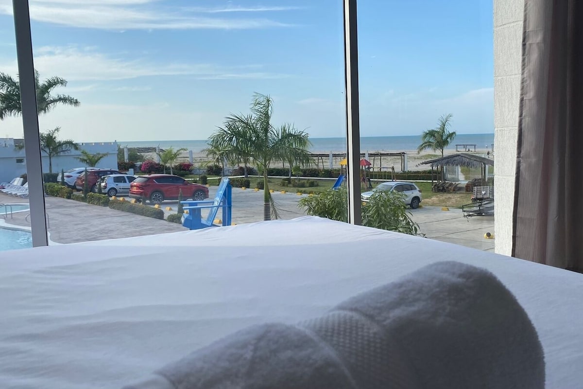 A hotel room with a large window overlooking a beach and parking area.