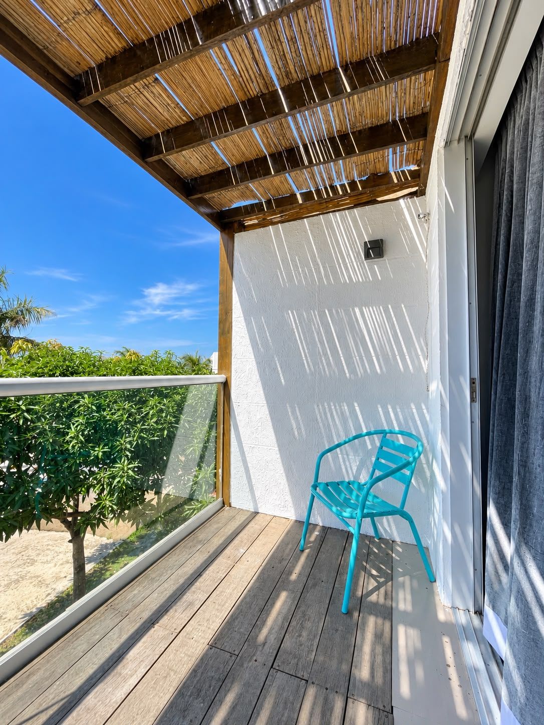 Un balcon doté d’un plancher en bois, d’une chaise bleue et offrant une vue sur la verdure.