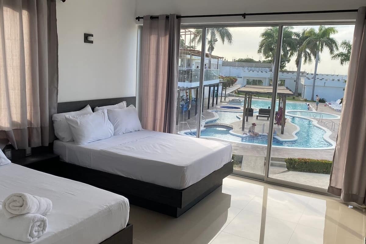 Habitación de hotel con dos camas, un ventanal con vistas a una piscina y palmeras.