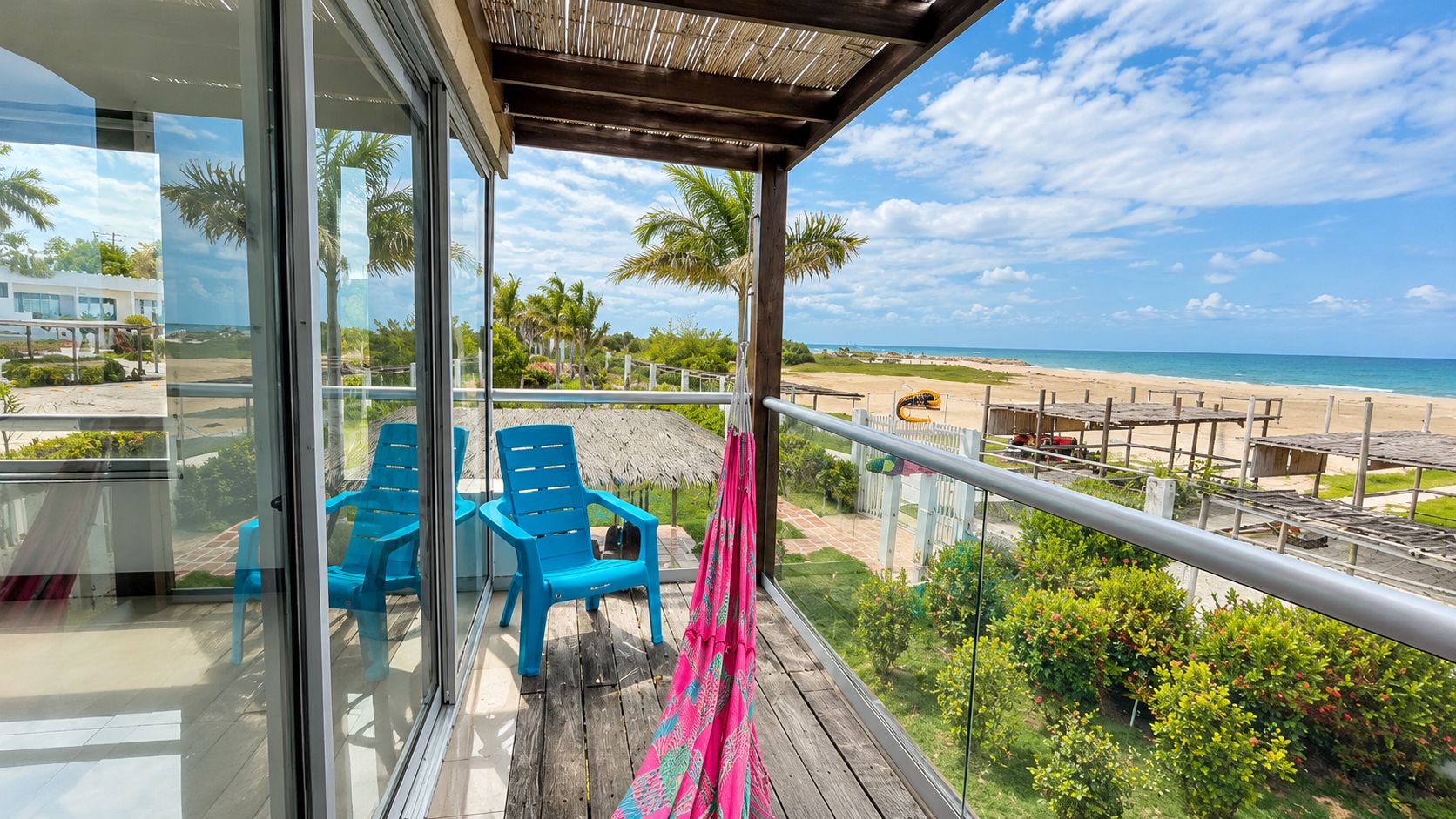 Un balcon avec vue sur la plage, des chaises bleues et une terrasse en bois.