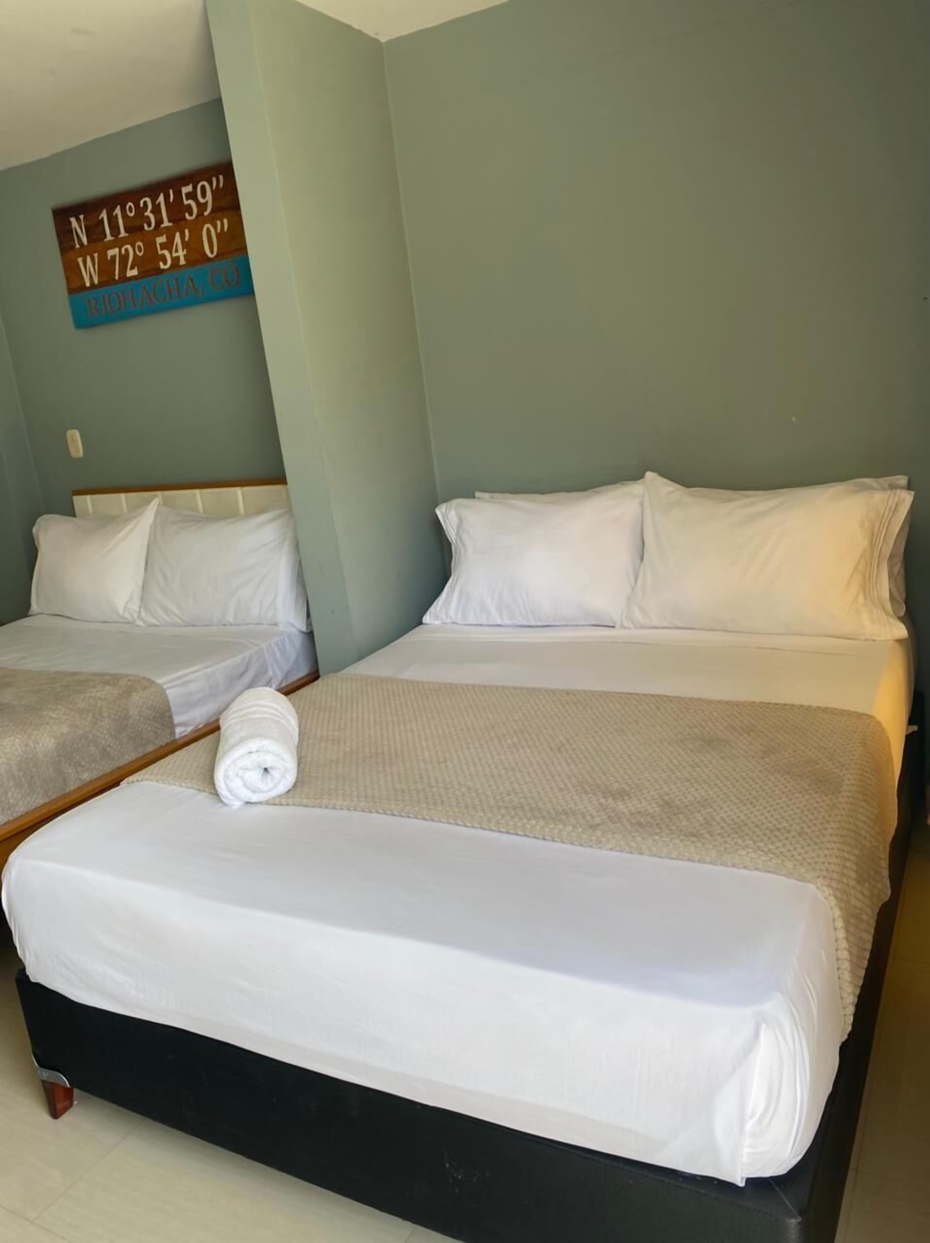 A hotel room with two beds, a wall clock, and a sign with coordinates.