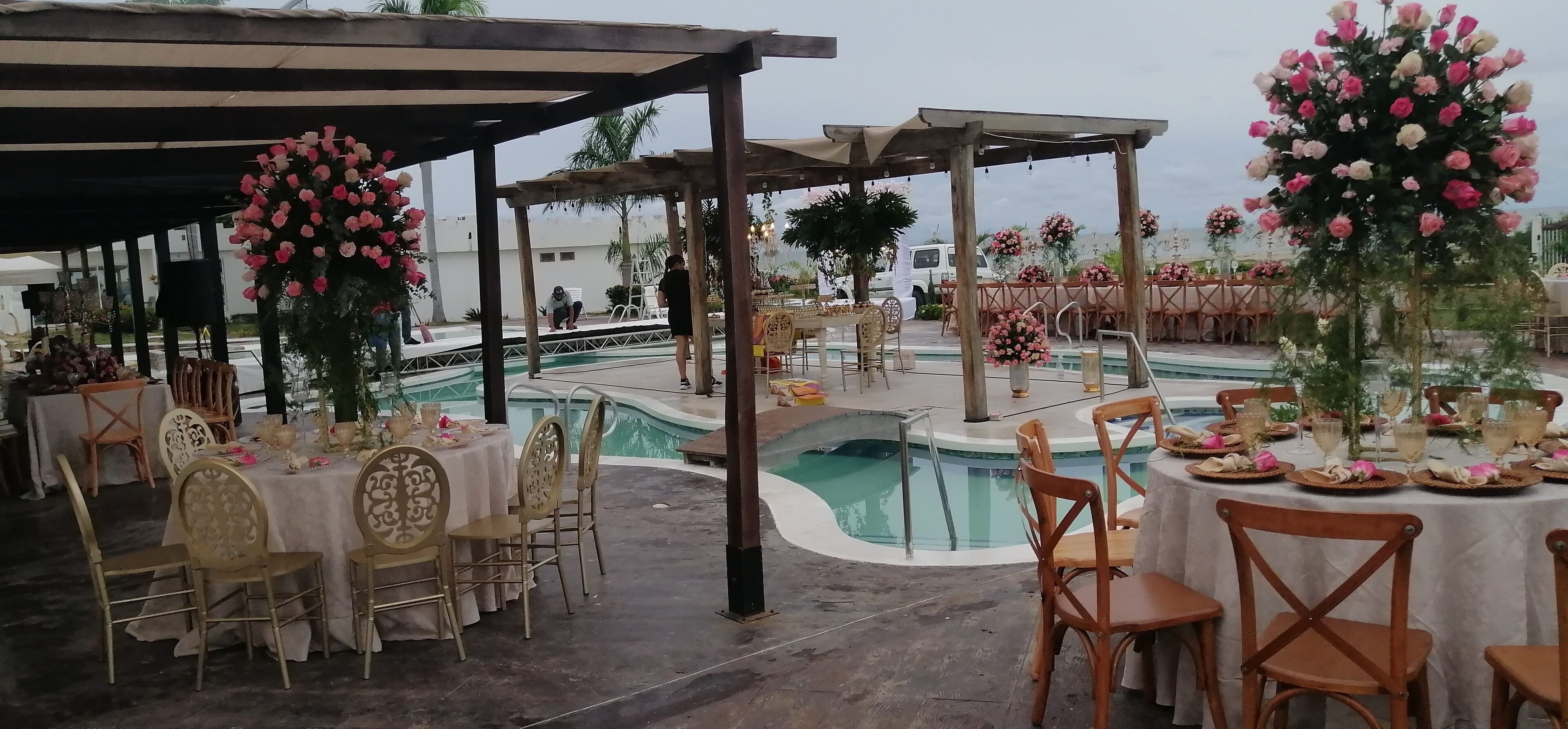 An outdoor event space with round tables and chairs, a pool, and floral decorations.