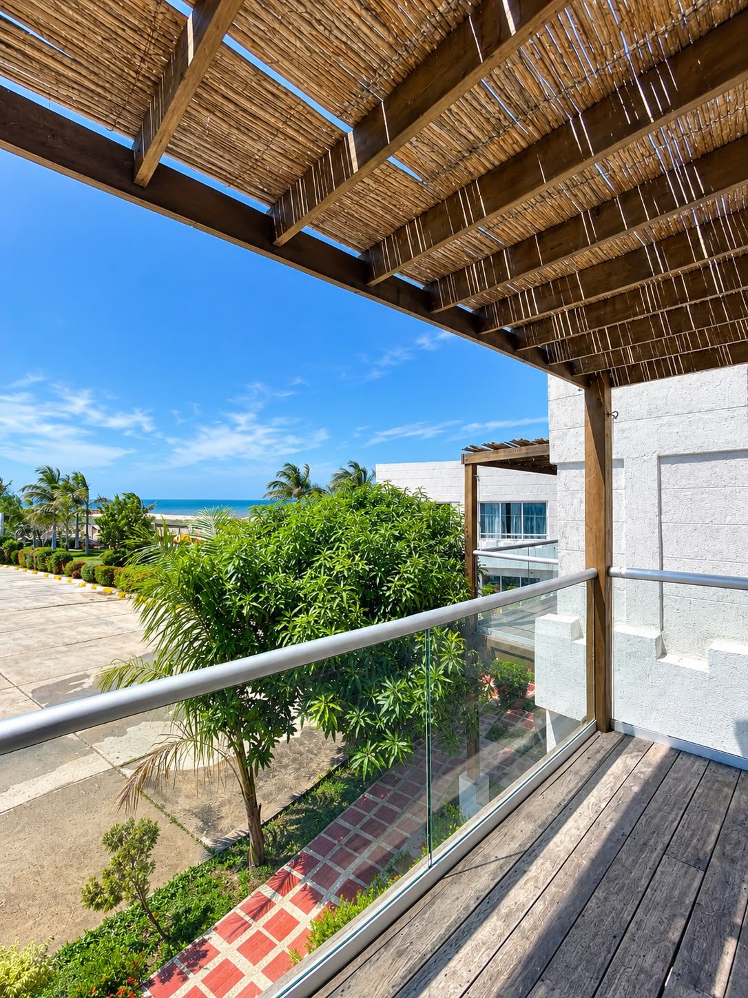 Un balcon doté d’une balustrade en verre, offrant une vue sur une plage et des palmiers.