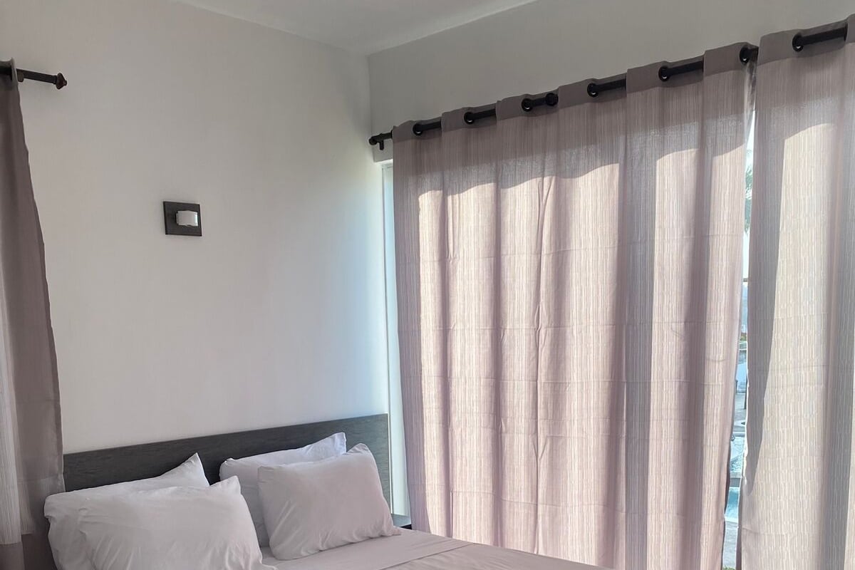 A modern hotel room with a large bed, dark headboard, and sheer curtains.