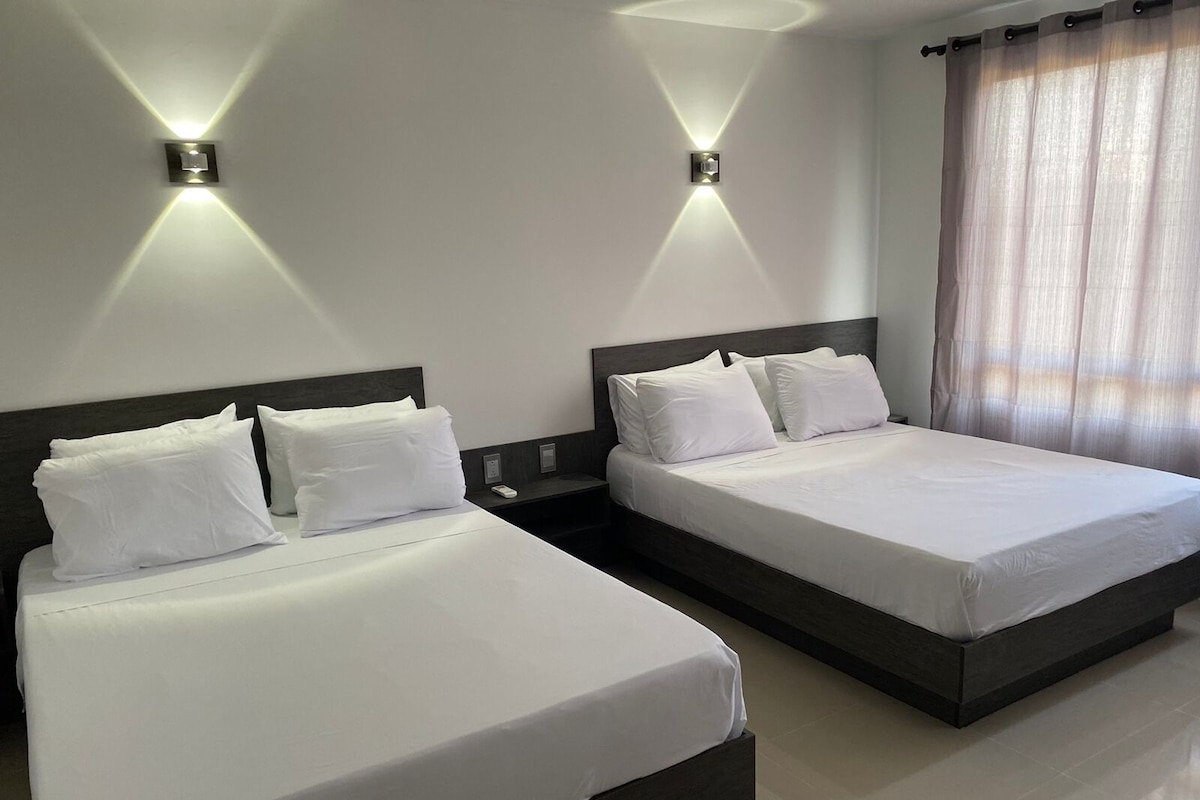 Two adjacent beds with white linens, a dark headboard, and a nightstand with a phone.
