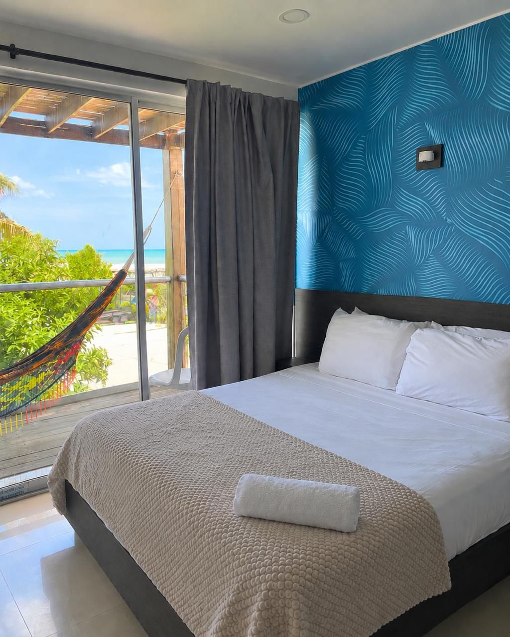 Une chambre d’hôtel avec un lit, une vue sur l’océan, un hamac et un mur orné d’un motif bleu.