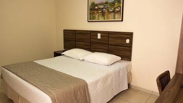 A neatly made bed with a wooden headboard, a bedside table, and a painting of a lakeside scene on the wall.