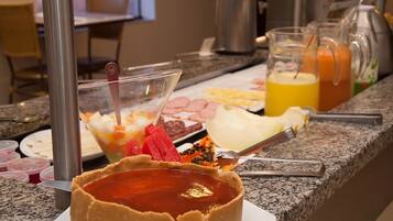 A buffet counter with various food items, including a tart in the foreground and a variety of dishes in the background.