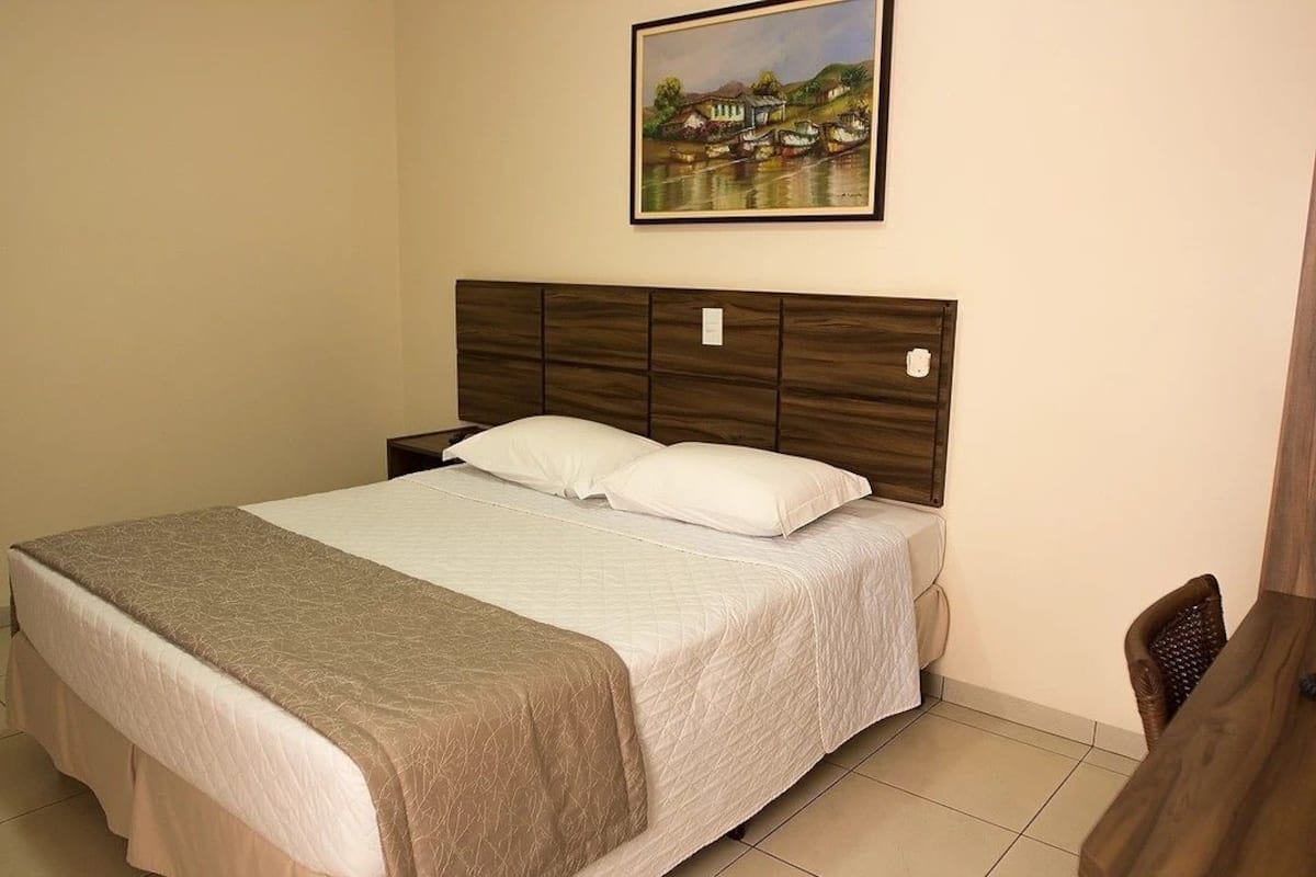 A neatly made bed with a headboard, a bedside table, and a chair.
