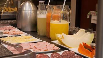 Un bufé con una variedad de carnes, quesos y frutas, junto con dos jarras de bebidas.