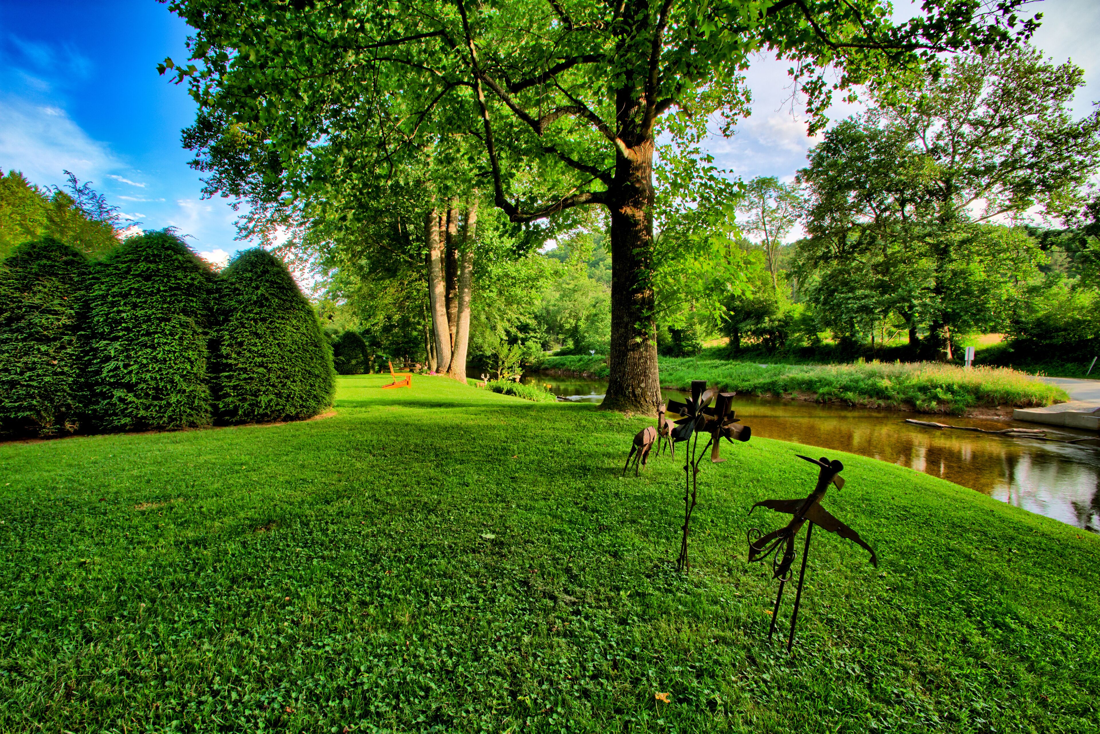 Lush, manicured grounds at Bridgepoint Cabin, where a peaceful creek winds past towering oaks and whimsical metal sculptures.