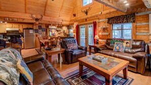 L’intérieur d’un chalet confortable en bois, avec un coin repas, une cheminée, des meubles en cuir et une grande fenêtre.