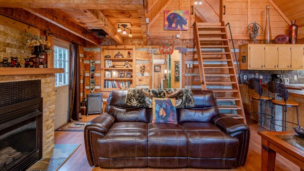L’intérieur chaleureux d’un chalet avec une cheminée, un canapé en cuir, des étagères en bois et un escalier menant à un étage supérieur.