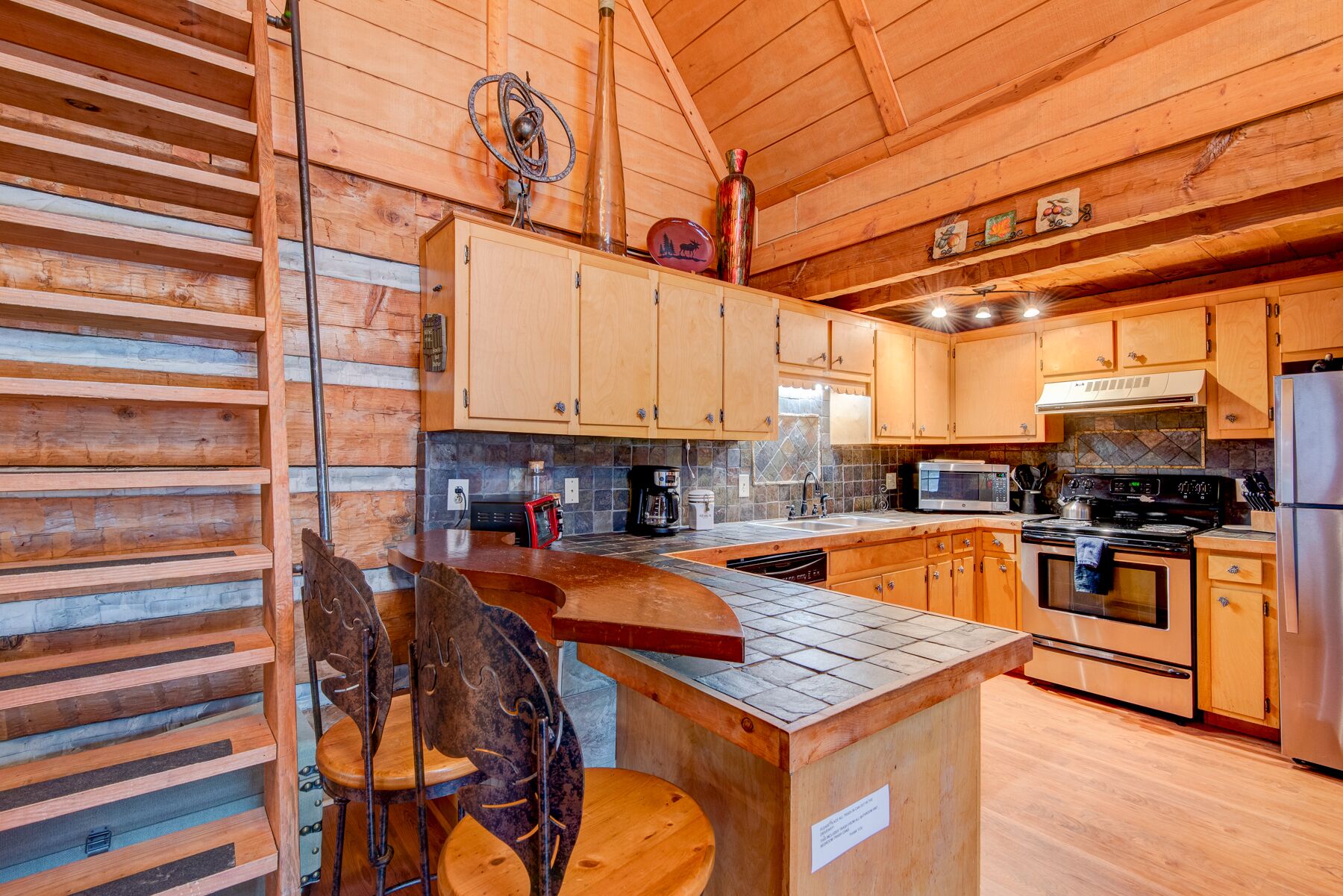 Interior de una cabaña de madera con cocina, que incluye armarios de madera, estufa, microondas y pileta.