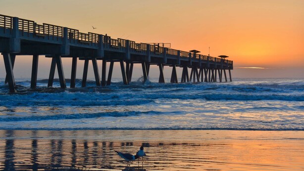 A pier extending into the ocean at sunset with waves crashing against it.