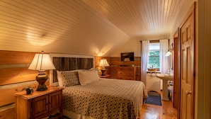 Um quarto aconchegante com teto de madeira, uma cama com colcha estampada, cômoda, televisão e janela com cortinas.