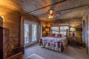 A wooden cabin bedroom with a bed, dresser, and ceiling fan.