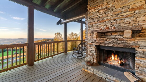 A stone fireplace with a fire, a wooden deck, and a view of the landscape. - Highland Mist  Pet Friendly, Beautiful Views, Hot Tub, Game Tables, Winery Close by (Banner Elk)