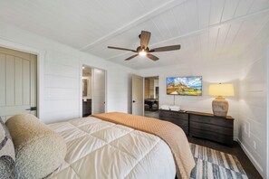 Une chambre à coucher avec un lit, un ventilateur de plafond, une commode, une lampe et un tableau accroché au mur.