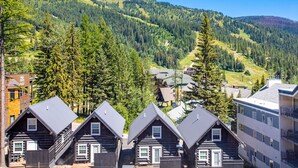 Blockhäuser mit Bergblick, umgeben von dichtem Wald und einem Skiort im Hintergrund.